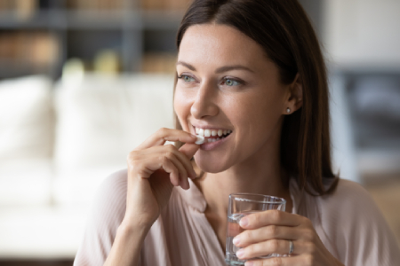Close up a mujer con vaso de agua y tomando una pastilla y sonriendo