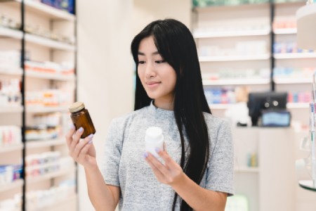 Mujer en pasillo de farmacia comparando frascos de multivitaminicos
